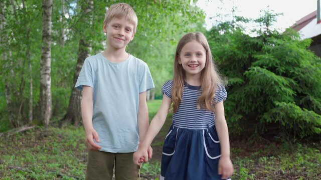 A boy and a girl hold each other's hand and smile. A boy loves a girl. The girl fell in love with the boy. Children's friendship. Falling in love in childhood. Romantic children. Charming smile
