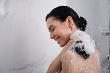 Young woman with mesh pouf taking shower at home. Space for text