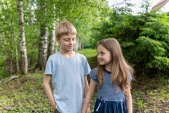 A boy and a girl hold each other's hand and smile. A boy loves a girl. The girl fell in love with the boy. Children's friendship. Falling in love in childhood. Romantic children. Charming smile summer