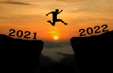 A young man jump between 2021 and 2022 years over the sun and through on the gap of hill ...
