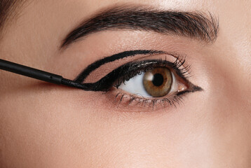 Beautiful woman applying black eyeliner, closeup view