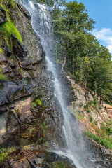 Naklejka na ściany i meble A stream of a waterfall flowing down a steep stone wall