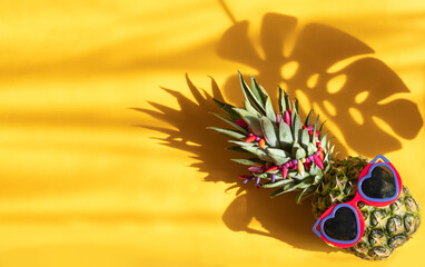 Pineapple hipster in sunglasses. Minimal concept, summer tropical pineapple.Hard shadows from the mostera leaf