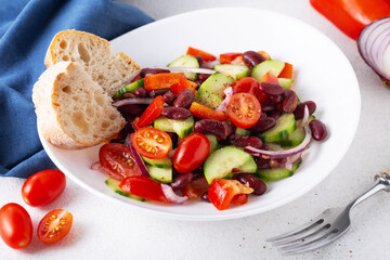 spanish salad with red beans and vegetables in a white plate, blue napkin, tomatoes, cucumbers, onions, ciabatta