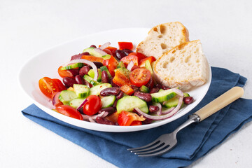 spanish salad with red beans and vegetables in a white plate, blue napkin, tomatoes, cucumbers,...