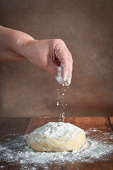 The hands of an elderly, plump woman are kneading dough on a wooden table. Preparation of dough for a festive cake, pizza