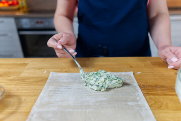 The process of making homemade snacks with cottage cheese and dill. The cook puts stuffing in to the dough.