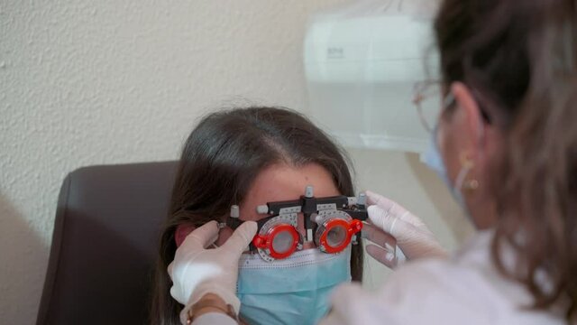 A girl during a pandemic, wearing a mask, does an exam with an ophtomologist, with myopia of vision. Special glasses for glass matching.