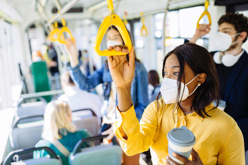 Pensive tired black woman commuting work by bus and wearing protective face mask due to coronavirus...