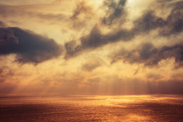 The sun's rays make their way through dramatic dark clouds over the sea, patches of light on the water