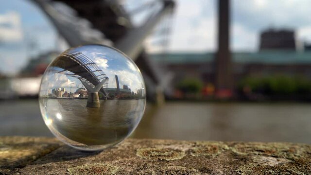 Tate Modern art gallery and the Millennium Bridge refracted in a glass sphere. Focus is on the refracted image. Shot from across the river.