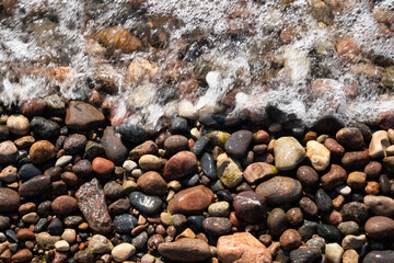 on the shores of the Baltic Sea there are stones of different colors, which form a beautiful pattern, where part of the image is covered by a foaming wave