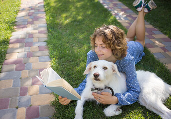 cute girl - teenager 17 - 18 years old lies on the grass next to her white dog, reading a book....