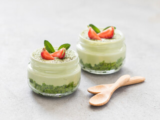 Dessert of spinach sponge cake with cottage cheese cream with green tea matcha with fresh strawberries in a glass jar on a light background