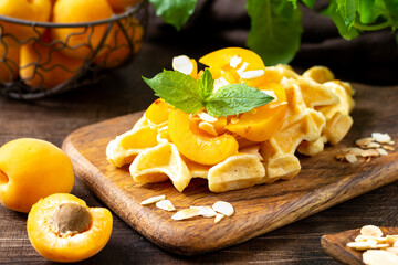 Traditional classic Belgian or Brussels waffles with apricots and almonds on a serving board on a brown wooden kitchen table closeup