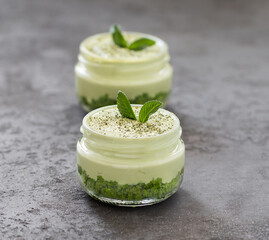 Obraz na płótnie Canvas Summer dessert of spinach biscuits with cottage cheese cream with green tea matcha in a glass jar on a dark gray background