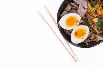 Top view studio shot of black bowl of ramen noodles with boiled eggs, veggies and turkey meet, ready to be poured with boiling broth and wooden chopsticks isolated on white background.