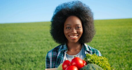 Multiracial female gardener smells and showing to the camera fresh tomatoes at the green plantation. Greenhouse expert, agronomy and bio farming concept