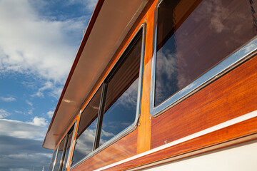 Wooden hull of a yacht with rectangular portholes against the sky, side view.
