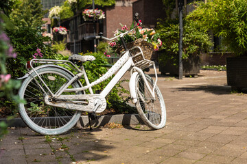 White parked bicycle with a basket and flowers inside in a green street in the center of Eindhoven...