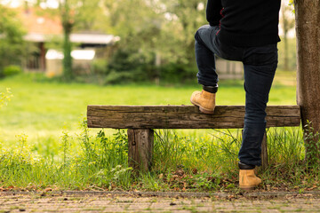 Man worker or farmer wearing casual clothes resting his foot on a rustic bench while looking over a green grassfield and relaxing, enjoying the nature outside on a sunny day during summer