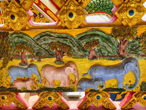 Stucco blue and pink elephants with colourful flowering trees and mountains in a Thai village temple in the province of Phetchabun.
