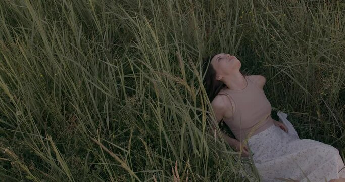 Pleasant dark haired woman in stylish outfit lying among high gress. Relaxation on fresh air during warm summer days. Connection with wild nature. 