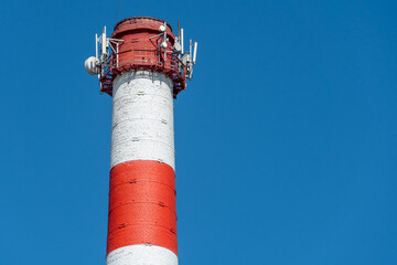 A large industrial smokestack against a blue sky. Red and white pipe in commercial enterprises or power plants.