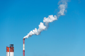 View of a thermal power plant or a factory for the production and processing of petroleum products. Large industrial chimneys against a clear blue sky. Removal of combustion