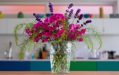 Vase of cut garden flowers, including pink sweet pea, lavender and wispy asparagus leaves. 