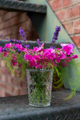 Vase of cut garden flowers, including pink sweet pea, lavender and wispy asparagus leaves. 