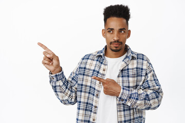 Confused african american man with moustache, pointing fingers and looking left at smth strange,...