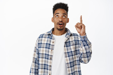 Handsome african american male model pointing, looking up with curious face, reading promo text, showing logo sale banner, standing against white background