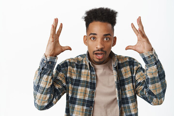 Fototapeta premium Boom, mindblown info. Shocked and surprised african american man show head explosion gesture, shaking hands near face and looking astonished at camera, white background