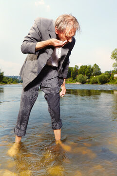 Manager in grey suit became crazy of hot weather and cooling in river