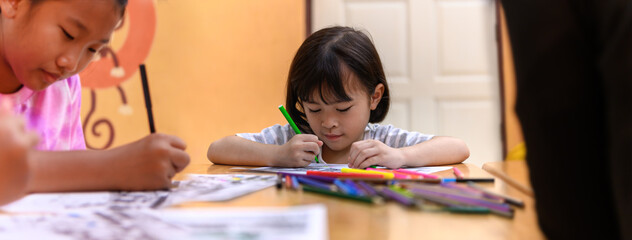 Asian little girl group sitting practice their skills and focus on coloring paper on table. Preschoolers learning at home to write and reading, Art education and creativity, Children's activities.