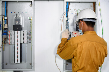 Electrician engineer using digital multimeter test current electric in control panel ​for testing electrical installations and wiring work in power control room on new building.