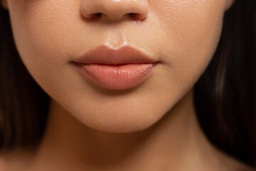 Naklejka premium Close-up of woman's lips with fashion natural beige lipstick makeup. Macro sexy pale lipgloss make-up . Gentle pure skin and wavy brunet hair. Cosmetology, Spa, increase in lips