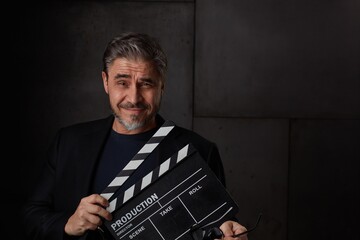 Happy movie director holding black clapper board. Movie director starting film. Copy space, dark background. - obrazy, fototapety, plakaty