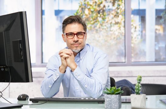 Businessman working in office with computer sitting at desk. Portrait of mature age, middle age, mid adult man in 40s.