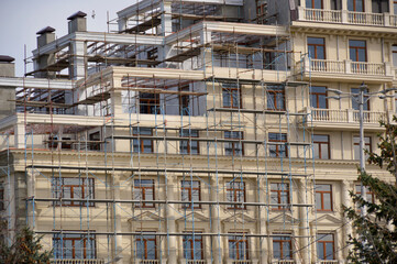 Fototapeta na wymiar the future facade of a multi-storey building is hidden behind scaffolding, the upper floors of the house are still being completed