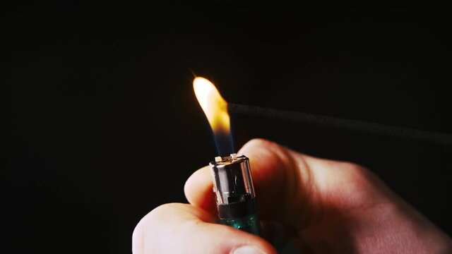 A man's hand holds a lighter that sets fire to an aroma stick