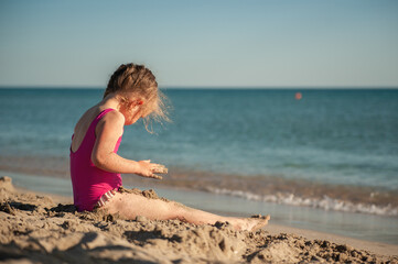 Cute little girl playing in the sand on the sea beach