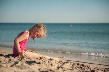 Fototapeta premium Cute little girl playing in the sand on the sea beach
