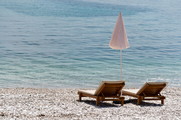 Wooden sun loungers under a sunshade on the seashore