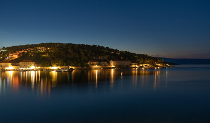 Night view of a very calm sea by the shore with a beautifully lit town in the background