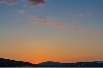 The sun just above the sea horizon creating a sunrise / sunset with a panorama of the mountains and rocky beaches