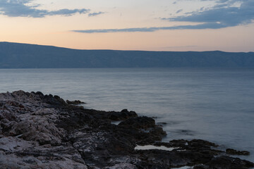 The sun just above the sea horizon creating a sunrise / sunset with a panorama of the mountains and rocky beaches