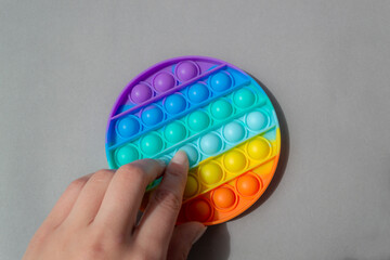 Bright colorful silicone Pop it toy. Popular anti-stress toy on a gray background, a female hand presses the bubbles