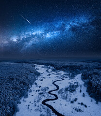 Milky way over frozen river and snowy forest in winter.